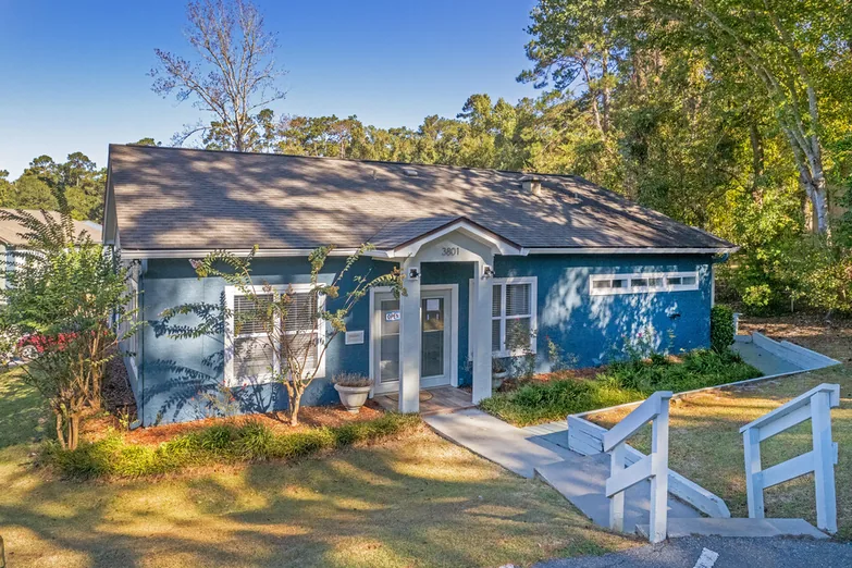 Blue two-story garden apartment building with mature trees at Crescent Ridge Apartments, Tallahassee